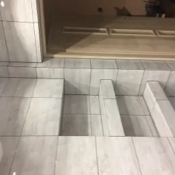 Wykończona wnęka z półkami, wyłożona jasnymi, marmurkowymi płytkami ceramicznymi, przylegająca do drzwi z drewnianą ościeżnicą.