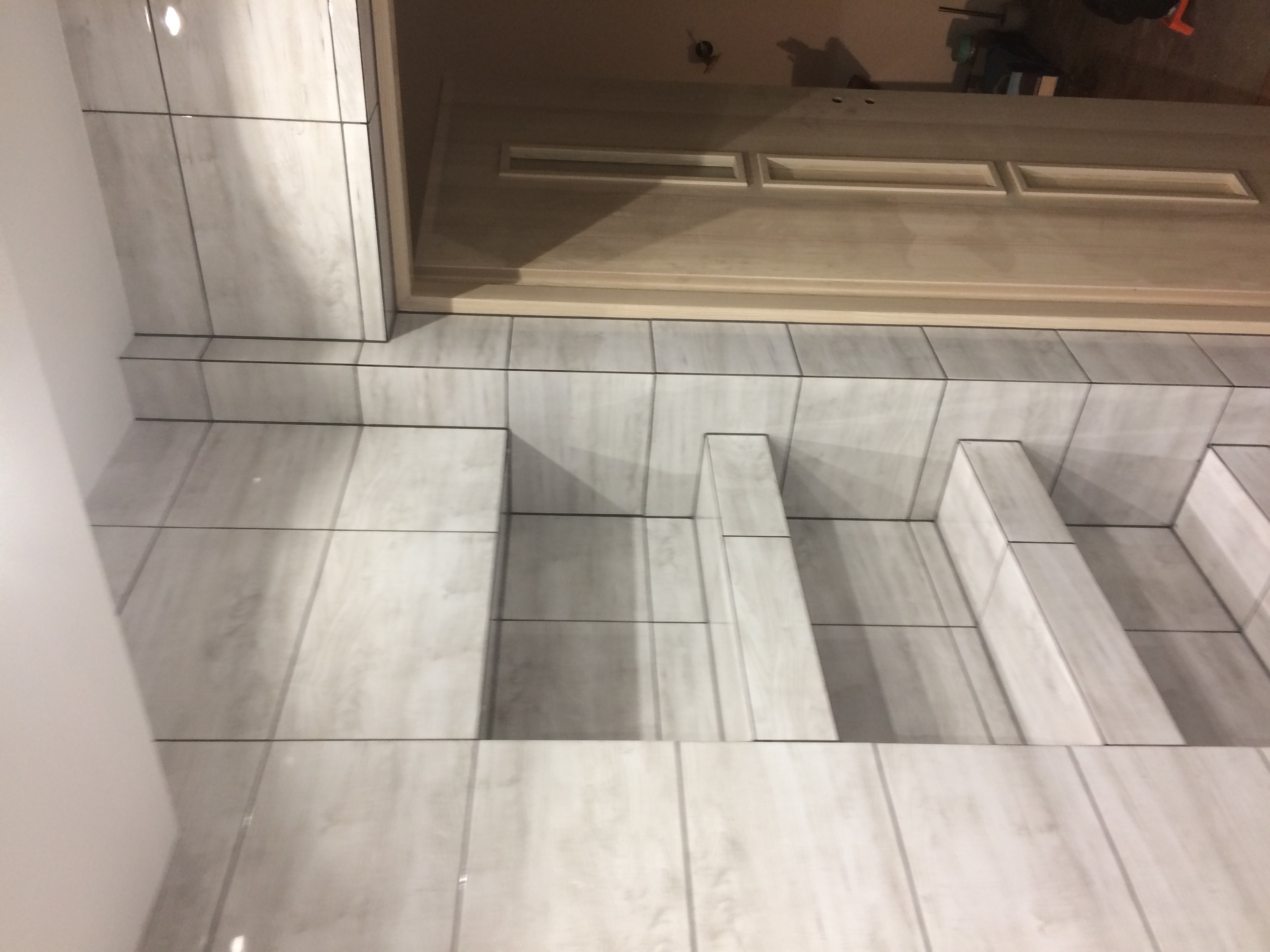 Wykończona wnęka z półkami, wyłożona jasnymi, marmurkowymi płytkami ceramicznymi, przylegająca do drzwi z drewnianą ościeżnicą.