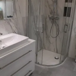 Nowoczesna łazienka z marmurowymi płytkami, białą szafką pod umywalkę z trzema szufladami, kabiną prysznicową narożną i pralką Samsung.