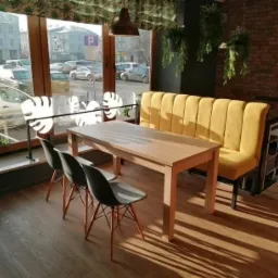 Wnętrze kawiarni z drewnianym stołem, trzema krzesłami i żółtą tapicerowaną ławką pod oknem z widokiem na ulicę.