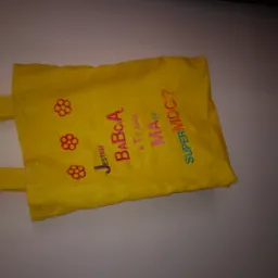 Żółta torba z lnu z haftowanymi napisami i motywami kwiatowymi, leżąca na jasnym tle.