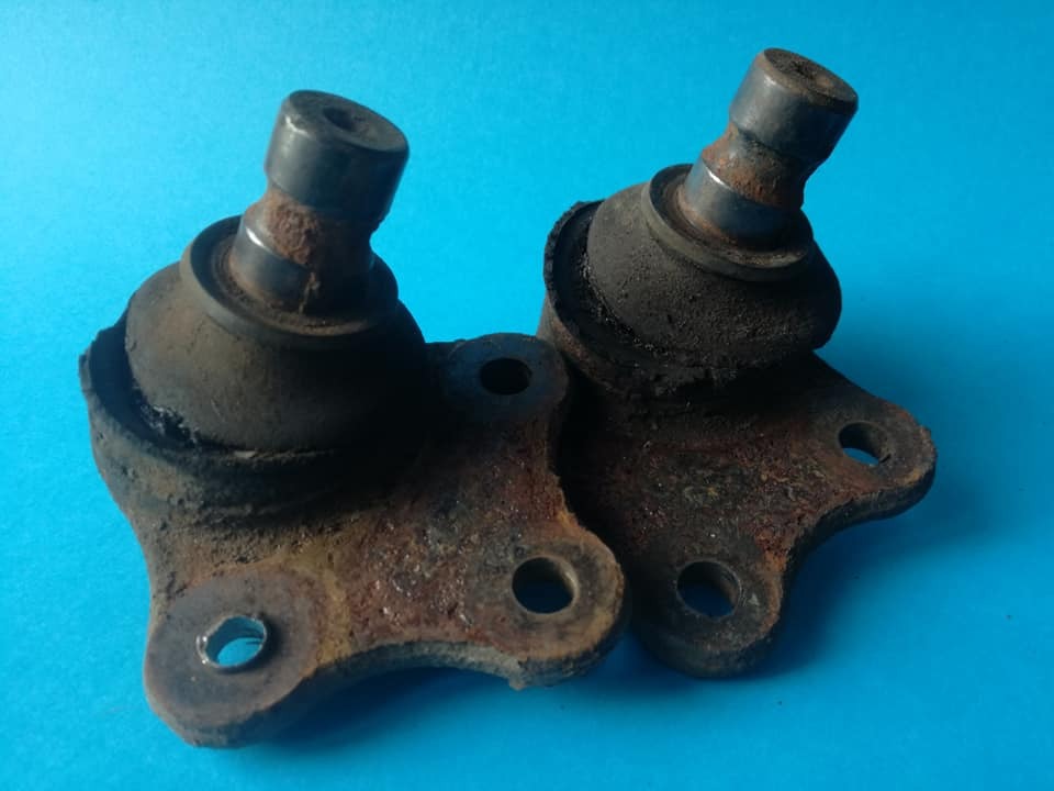 Dwa skorodowane sworznie wahacza na niebieskim tle, widoczne ślady zużycia i rdzy.