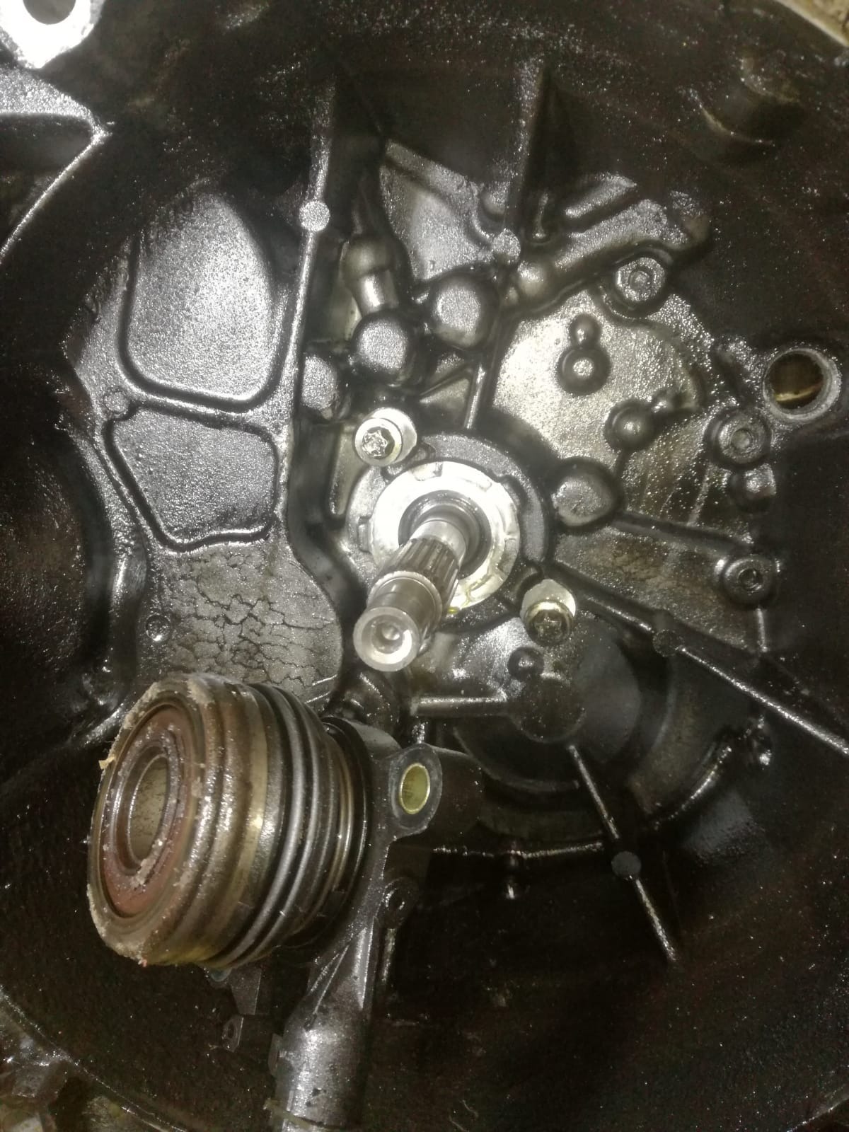 Wnętrze skrzyni biegów, widoczny wysprzęglik sprzęgła i wałek, elementy pokryte olejem, widoczne ślady użytkowania.