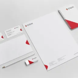 Komplet materiałów biurowych marki SIGNI: wizytówki, papier firmowy, koperta, notatnik spiralny, ołówek i gumka, wszystko w kolorystyce biało-czerwonej, ułożone na jasnym tle, prezentacja...