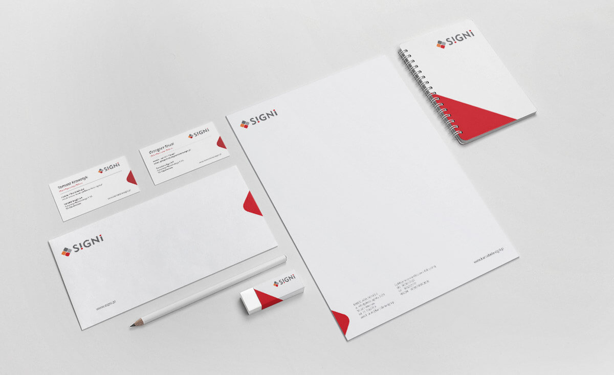 Komplet materiałów biurowych marki SIGNI: wizytówki, papier firmowy, koperta, notatnik spiralny, ołówek i gumka, wszystko w kolorystyce biało-czerwonej, ułożone na jasnym tle, prezentacja...
