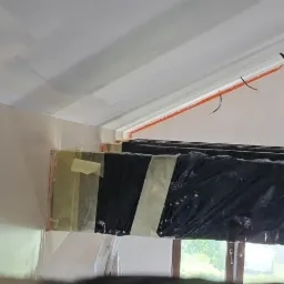 Przygotowanie do malowania poddasza: zabezpieczone okna folią, ściany i sufit po szpachlowaniu, widoczne przewody elektryczne, taśma malarska w narożnikach.