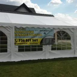 Rozłożony biały namiot bankietowy z reklamą firmy na tle domu i trawnika.