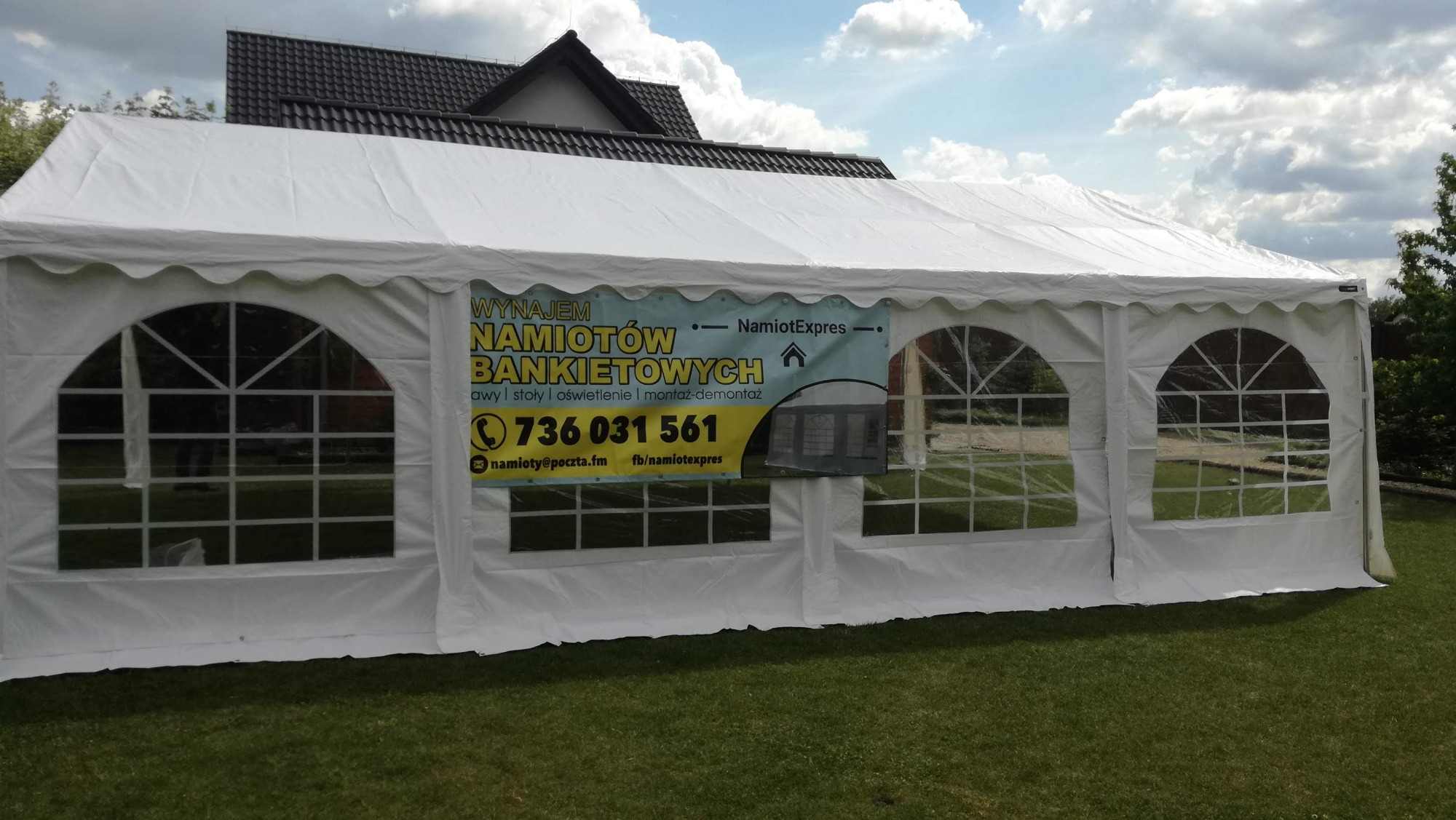 Rozłożony biały namiot bankietowy z reklamą firmy na tle domu i trawnika.