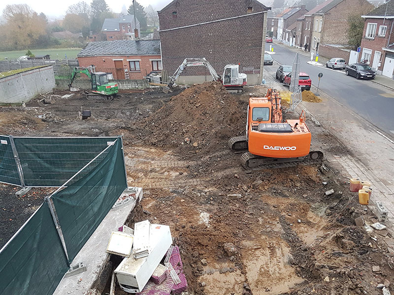 Plac budowy z kilkoma koparkami, w tym pomarańczową Daewoo, przygotowujący teren pod budowę w zabudowie miejskiej, widok z góry.