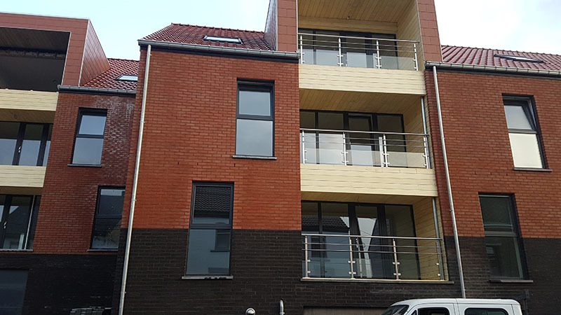 Nowoczesny budynek wielorodzinny z cegły w Łęczycy, z balkonami z metalowymi balustradami i dużymi oknami, część elewacji w ciemnym kolorze.