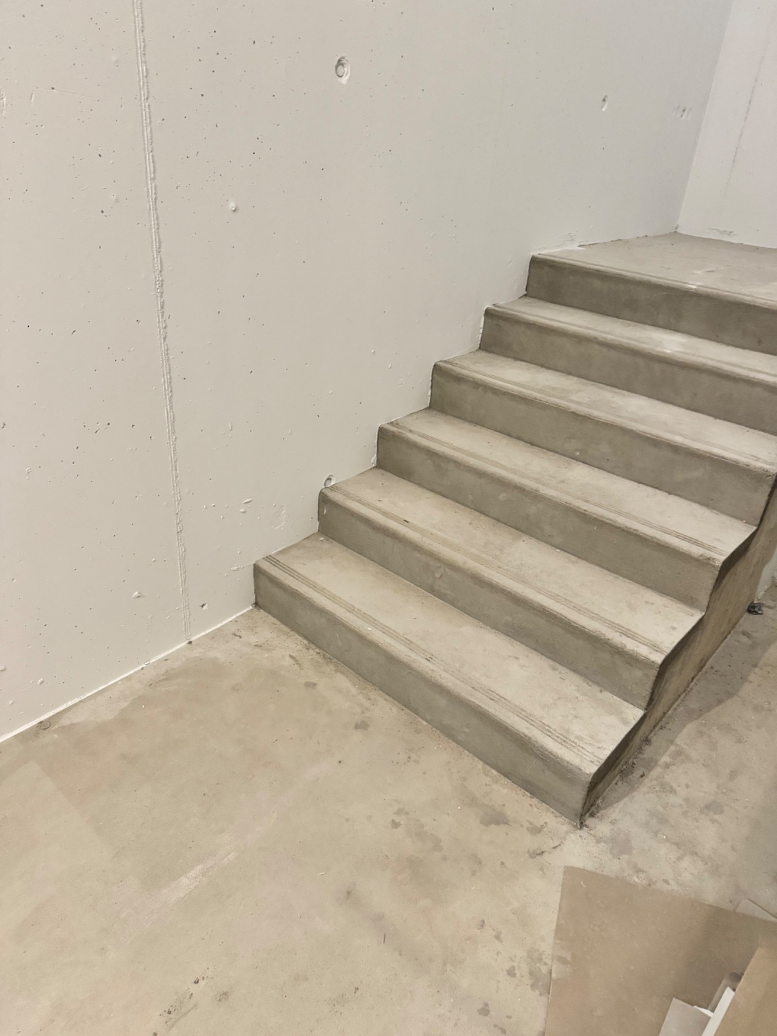 Surowe betonowe schody w trakcie prac wykończeniowych, widoczne ślady po szpachlowaniu na ścianie i podłodze, minimalistyczne wnętrze.