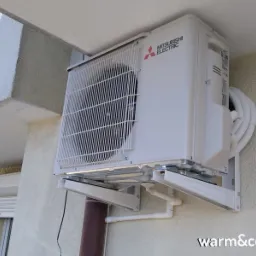 Zewnętrzna jednostka klimatyzacji Mitsubishi Electric zamontowana na ścianie budynku, widoczne rury i wsporniki montażowe.