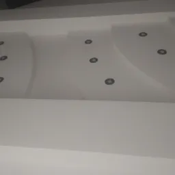 Nowoczesny biały sufit podwieszany z segmentami w kształcie łuków i zamontowanymi punktowymi oprawami oświetleniowymi.