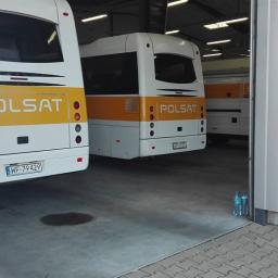 SZORUJ.PL SPÓŁKA Z OGRANICZONĄ ODPOWIEDZIALNOŚCIĄ - Wnętrze hali garażowej z trzema autobusami marki Polsat, widoczne tylne światła i tablice rejestracyjne, na podłodze widoczne ślady oleju i dwie butelki wody mineralnej.