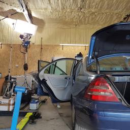 SZORUJ.PL SPÓŁKA Z OGRANICZONĄ ODPOWIEDZIALNOŚCIĄ - Niebieski samochód z otwartymi drzwiami i bagażnikiem w warsztacie z oświetleniem studyjnym, widoczny podnośnik samochodowy i komputer.