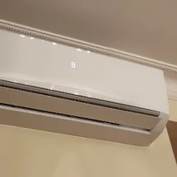 Biała jednostka klimatyzacji marki Gree zamontowana na ścianie z wyświetlonym numerem 8, widoczna listwa dekoracyjna pod sufitem.