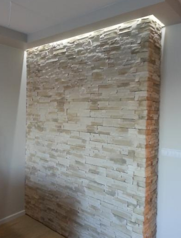 Ściana wewnętrzna wykończona dekoracyjną okładziną z jasnego kamienia z podświetleniem LED w górnej części, tworząca nowoczesny akcent w pomieszczeniu.