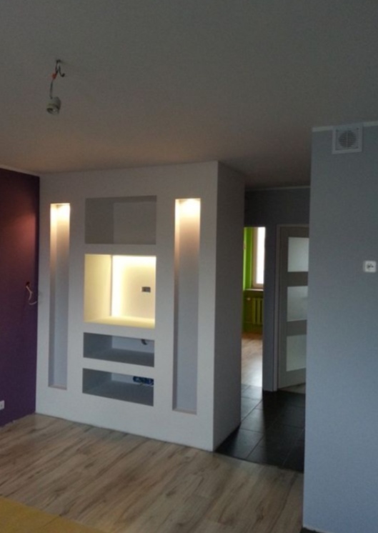 Nowoczesna ścianka działowa z oświetleniem LED w Częstochowie, z półkami i wnękami, na tle fioletowej ściany i parkietu.