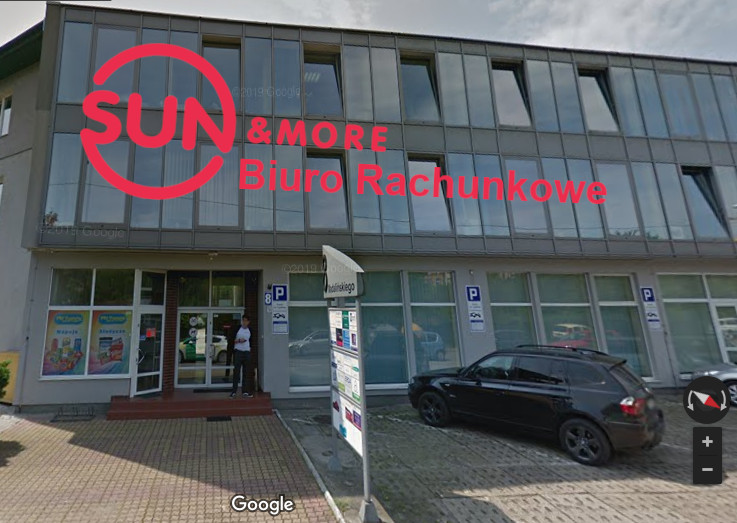 Dwupiętrowy budynek z dużymi oknami, na którym widnieje napis 'SUN & MORE Biuro Rachunkowe', przed budynkiem zaparkowany czarny samochód, na chodniku stoi osoba.