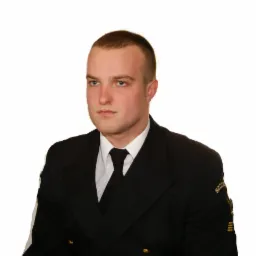 Portret mężczyzny w czarnym mundurze z naszywką 'SZCZECIN' na ramieniu, na białym tle.