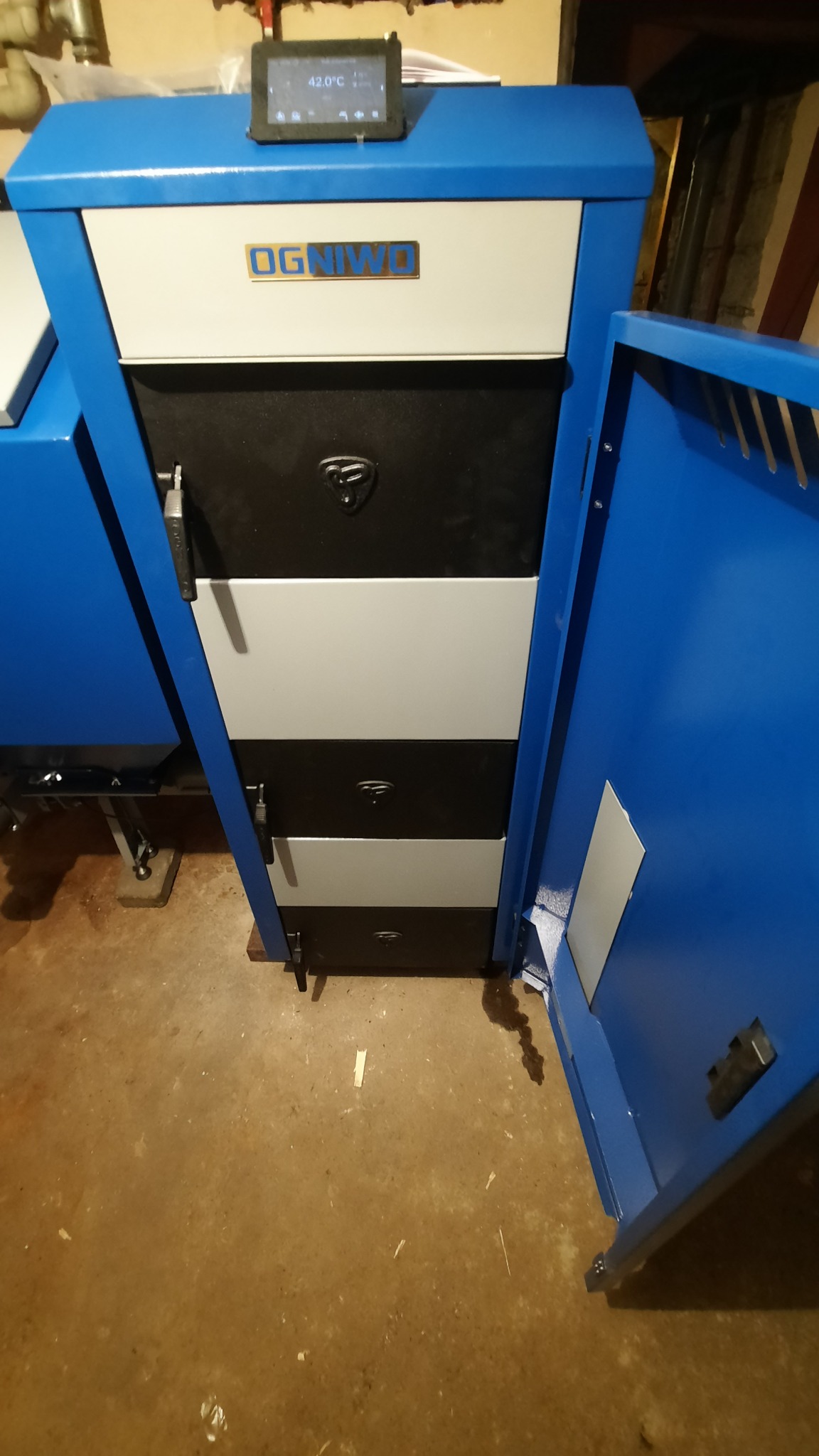 Niebiesko-biały piec CO marki Ogniwo z otwartymi drzwiczkami, temperatura wyświetlana na ekranie to 42 stopnie Celsjusza.