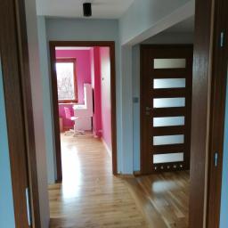 Hadson - Widok na korytarz z drewnianą podłogą i trzema parami drzwi w Zduńskiej Woli. Jedne drzwi z przeszkleniami, drugie prowadzą do różowego pokoju z biurkiem.