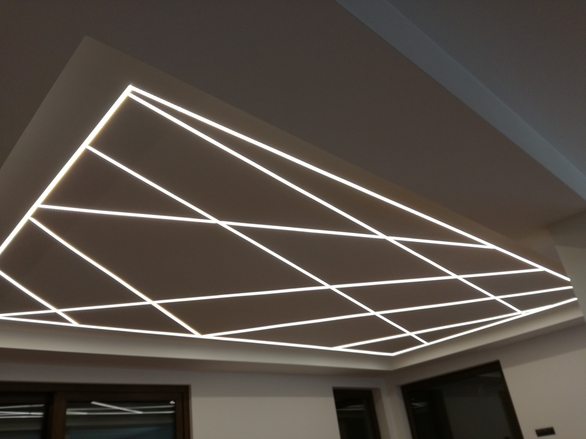 Sufit podwieszany z geometrycznym wzorem z podświetlanych listew LED, tworzący nowoczesny design wnętrza.