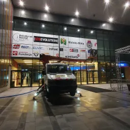 Montaż wielkoformatowej reklamy w Krakowie na szklanej fasadzie budynku, widoczny podnośnik koszowy z pracownikami na wysokości.