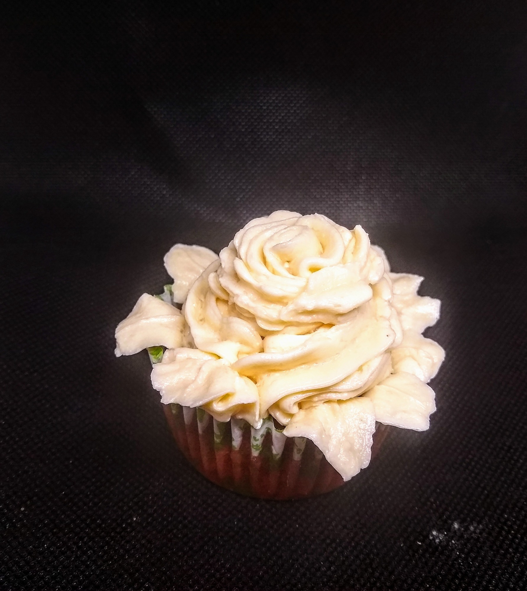 Pojedynczy babeczka z kremem w kształcie róży na ciemnym tle.