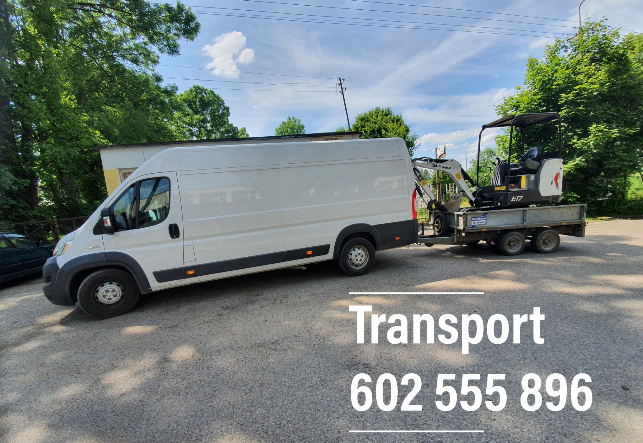 Biały bus z przyczepą przewożącą małą koparkę Bobcat E17 na tle zieleni i błękitnego nieba.