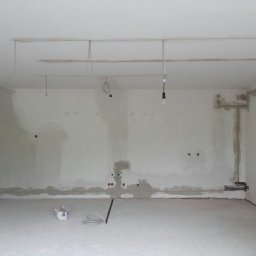 MODERN - TECH Technika domów - Wnętrze w trakcie remontu: surowe ściany z widocznymi punktami instalacji elektrycznej, wiszące przewody, drabina aluminiowa i wiadro z zaprawą na podłodze.