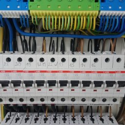 MODERN - TECH Technika domów - Rozdzielnica elektryczna z bezpiecznikami ABB, oznaczona numerami i podłączona kolorowymi przewodami, zamontowana w białej obudowie.