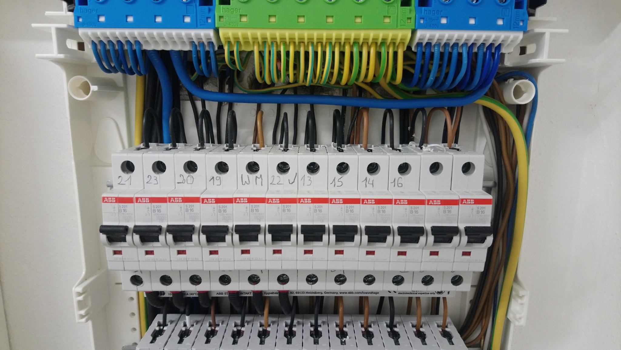 Rozdzielnica elektryczna z bezpiecznikami ABB, oznaczona numerami i podłączona kolorowymi przewodami, zamontowana w białej obudowie.