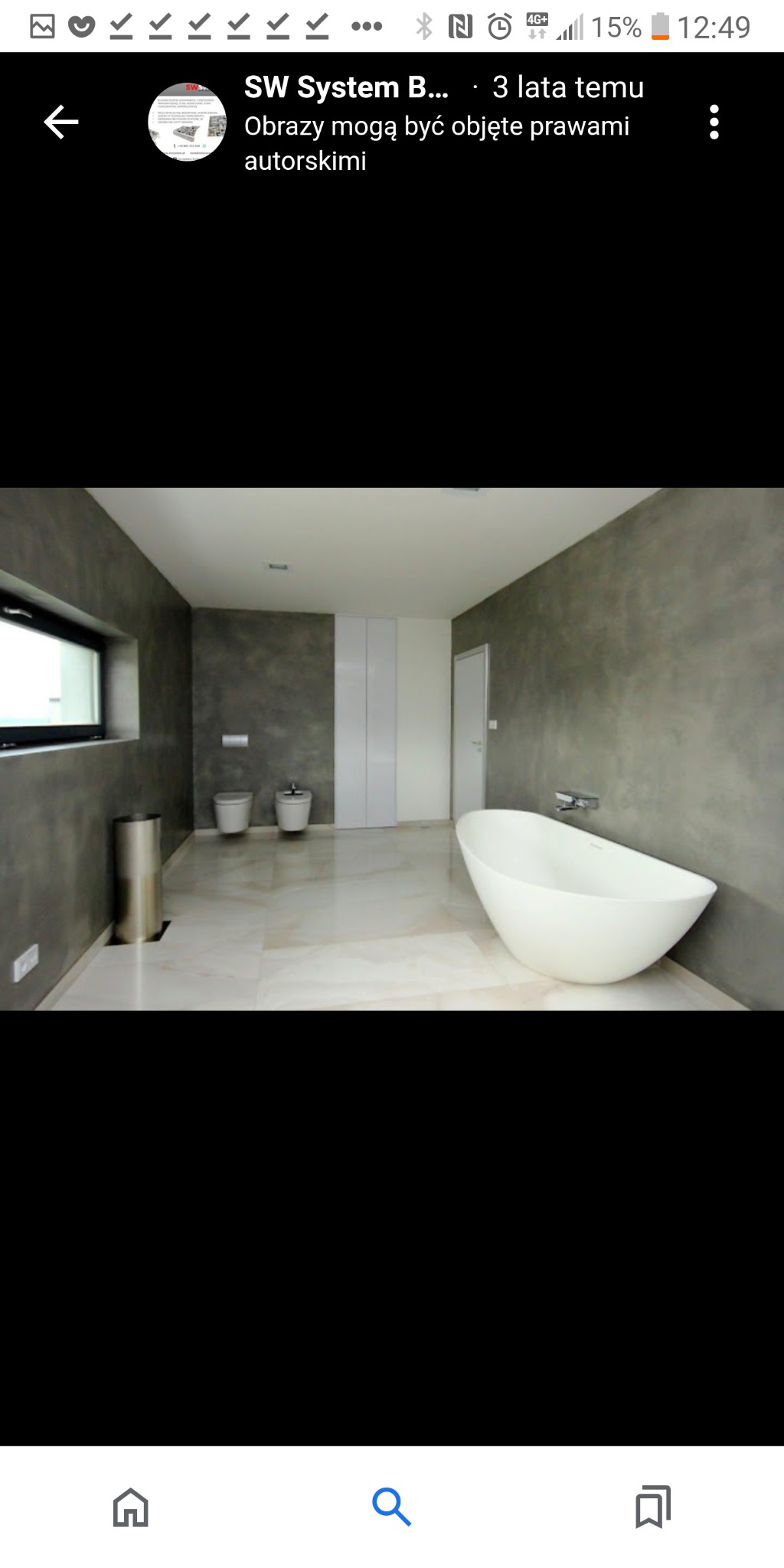 Nowoczesna łazienka z szarymi ścianami o fakturze betonu, wolnostojąca biała wanna, marmurowe płytki podłogowe, minimalistyczna armatura i ukryta podtynkowa bateria, podwieszana toaleta i bidet...