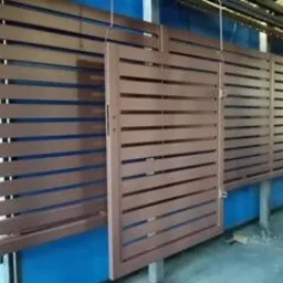 Brązowa, przesuwna brama z poziomych profili, widoczna na tle niebieskiej ściany w hali produkcyjnej.