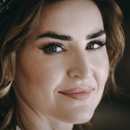 Foto Studio Andrzej Barełkowski - Portret kobiety z delikatnym makijażem i ozdobą we włosach, uśmiechająca się, z bliska, z ostrością na oczy i subtelne światło.