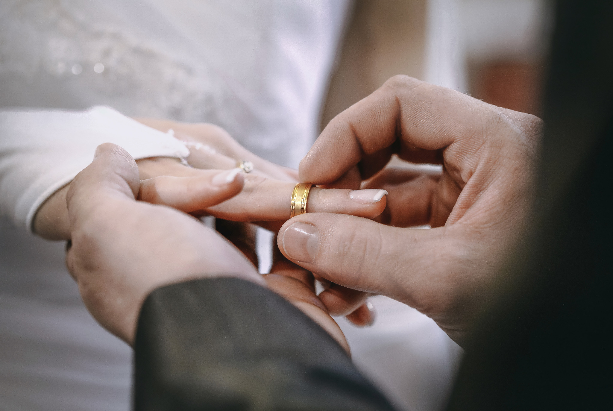 Zakładanie obrączki podczas ceremonii ślubnej we Wschowie. Dłonie w zbliżeniu, widoczna złota obrączka i fragment sukni panny młodej. Delikatne światło.