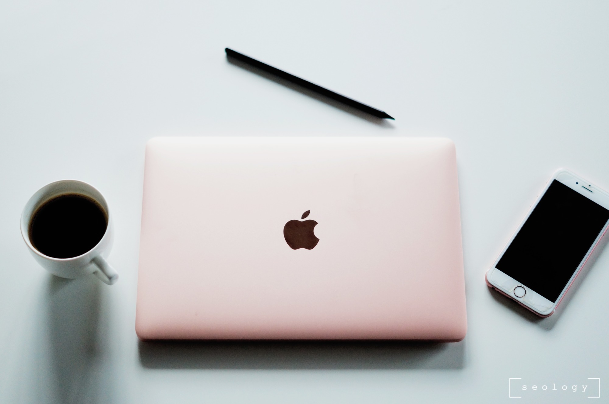 Różowy laptop, czarny rysik, biały smartfon i filiżanka kawy na białym tle, ujęcie z góry.