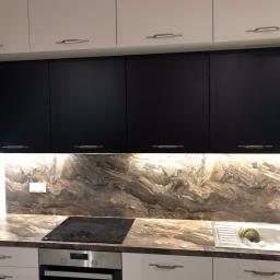 Przepis na kuchnie - Nowoczesna kuchnia z białymi i czarnymi szafkami, blatem imitującym marmur i podświetlanym panelem ściennym z motywem marmuru, z widoczną płytą indukcyjną i zlewem.