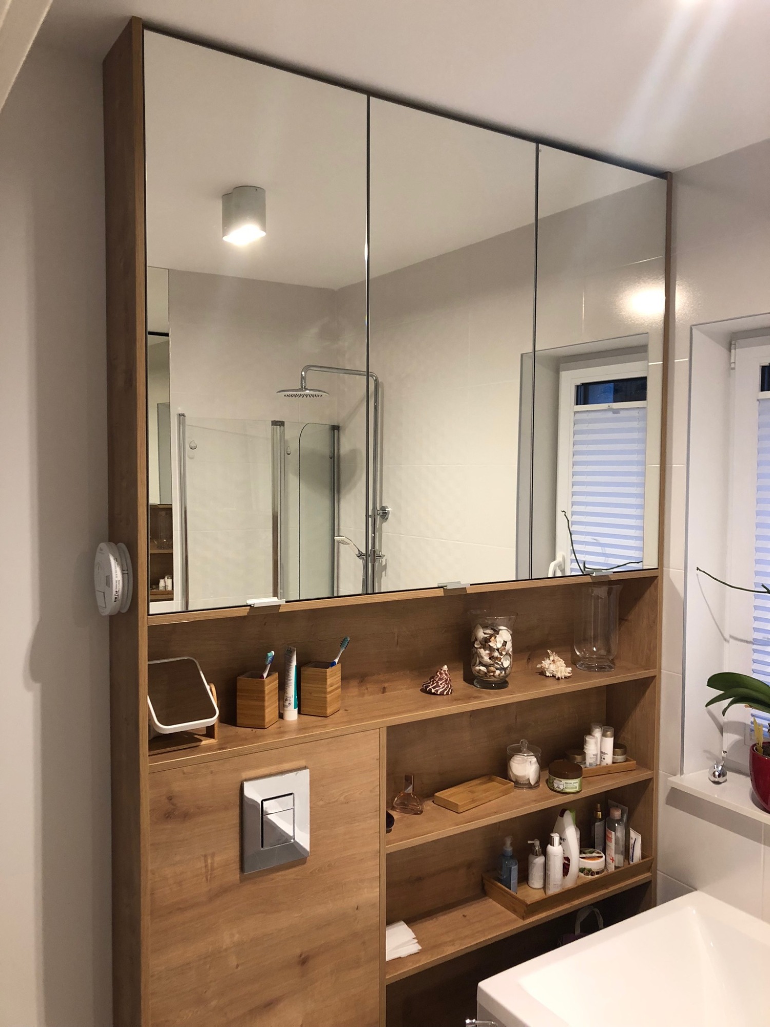 Nowoczesna łazienka z szafką z lustrami i drewnianymi półkami, widoczne akcesoria łazienkowe i elementy dekoracyjne