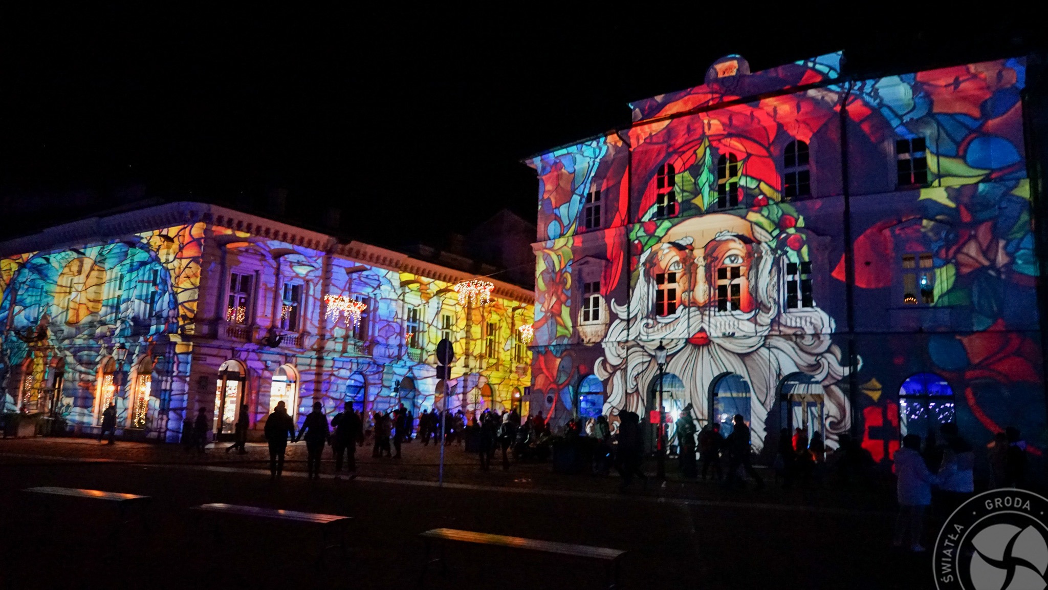 Budynki oświetlone kolorowymi projekcjami świetlnymi, przedstawiającymi motywy świąteczne i postać Świętego Mikołaja, widziane nocą.