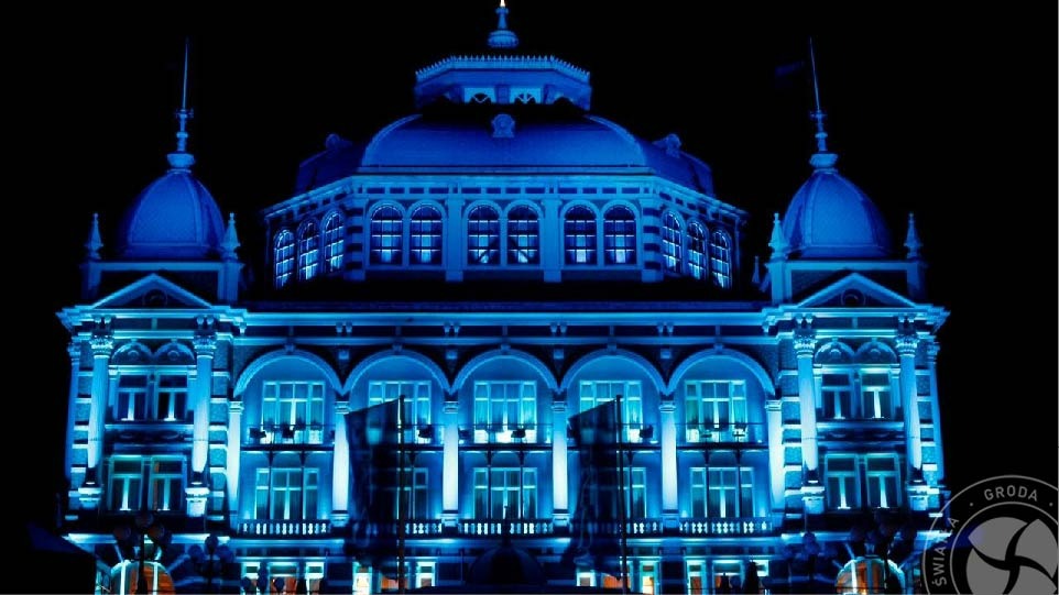 Elewacja budynku oświetlona intensywnym, jednolitym niebieskim światłem, nocne ujęcie z widocznymi kolumnami i detalami architektonicznymi.