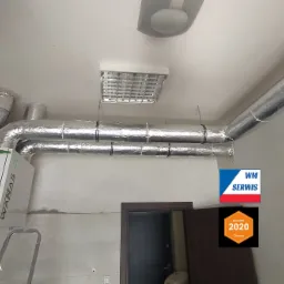 Zamontowany rekuperator WANAS z izolowanymi przewodami wentylacyjnymi na suficie, widoczny również fragment drabiny i logo firmy WM Serwis oraz nagroda Oferteo Najlepsi 2020.