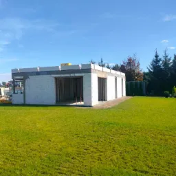 Budowa parterowego budynku w stanie surowym otwartym z białych bloczków, widoczne nadproża i otwory okienne, na dachu bloczki Ytong, zielony trawnik dookoła, Smolec.