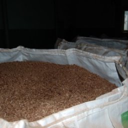 PHU BIALENERGO Olga Choińska - Pełen worek brązowych granulek w magazynie, widoczne okno w tle i inne worki.