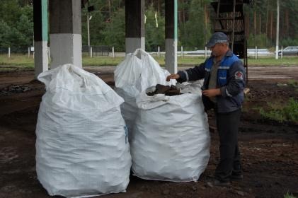 Mężczyzna w uniformie sprawdza zawartość worka z ciemnym materiałem na tle trzech dużych, białych worków pod zadaszeniem.