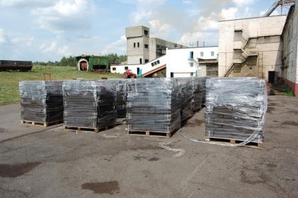 Sztaple brykietu drzewnego, owinięte folią i ułożone na paletach, zlokalizowane na placu firmy w Choroszczy. W tle budynki przemysłowe i fragment zieleni.