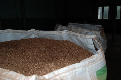 Pełen worek brązowych granulek w magazynie, widoczne okno w tle i inne worki.