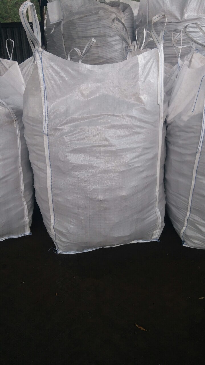 Duże, białe worki z zawartością, ułożone obok siebie, z widocznymi uchwytami do przenoszenia i niebieskimi szwami, stojące na ciemnej, prawdopodobnie betonowej powierzchni.