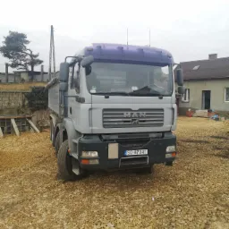 Szary samochód ciężarowy marki MAN na placu budowy z wysypanym kruszywem, widoczny numer rejestracyjny SO 8704T